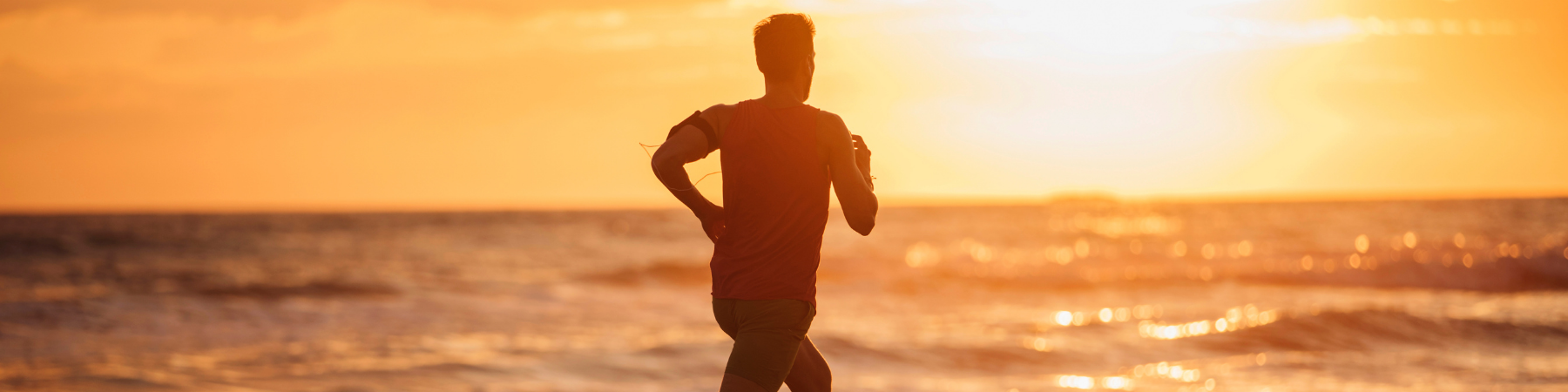 Man running at beach, looking at breathtaking sunset over the horizon